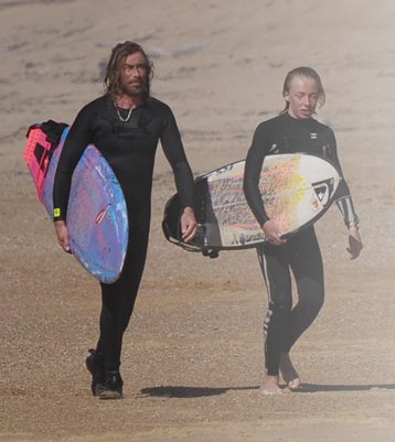 Nadixion en combinaison, planche de surf sous le bras, sur la plage